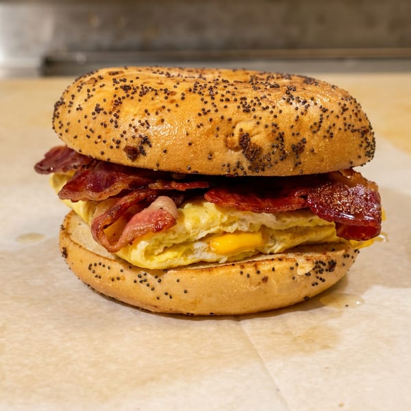 Poppy seed bagel with bacon, scrambled eggs, and cheese on parchment paper.