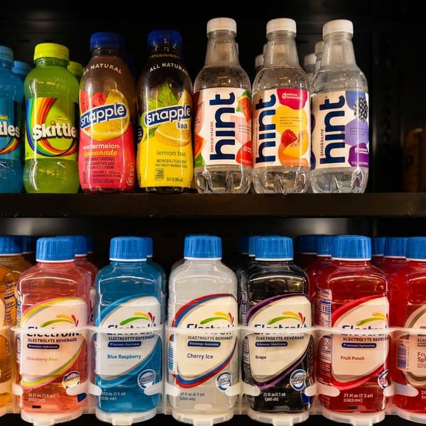 A refrigerated display case filled with colorful bottled beverages, including Skittles, Snapple, Hint, and Electrolit.